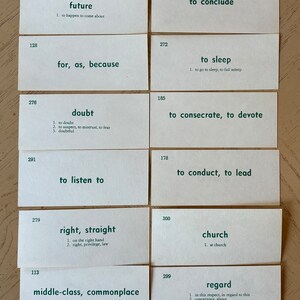Op de afbeelding: Een set van 16 witte indexkaarten met groene tekst. Elke kaart heeft een nummer en een woord of zin met een definitie. De woorden en zinnen omvatten "straat", "bidden, vragen, smeken", "toekomst", "want, zoals, omdat", "twijfel", "luisteren", "recht, recht", "middenklasse, alledaags", "branden", "redden", "volgen", "bureau, kantoor", "concluderen", "slapen", "wijden, wijden", "leiden, leiden", "kerk", "aandacht", "de fles", "schoorsteen, open haard".