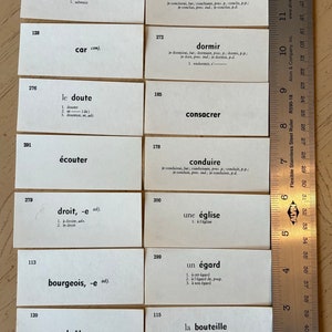Op de afbeelding: Een set witte indexkaarten met Franse woorden en definities. De kaarten zijn genummerd en in rijen gerangschikt. De woorden zijn in zwarte inkt gedrukt. Een liniaal is zichtbaar aan de onderkant van de afbeelding.