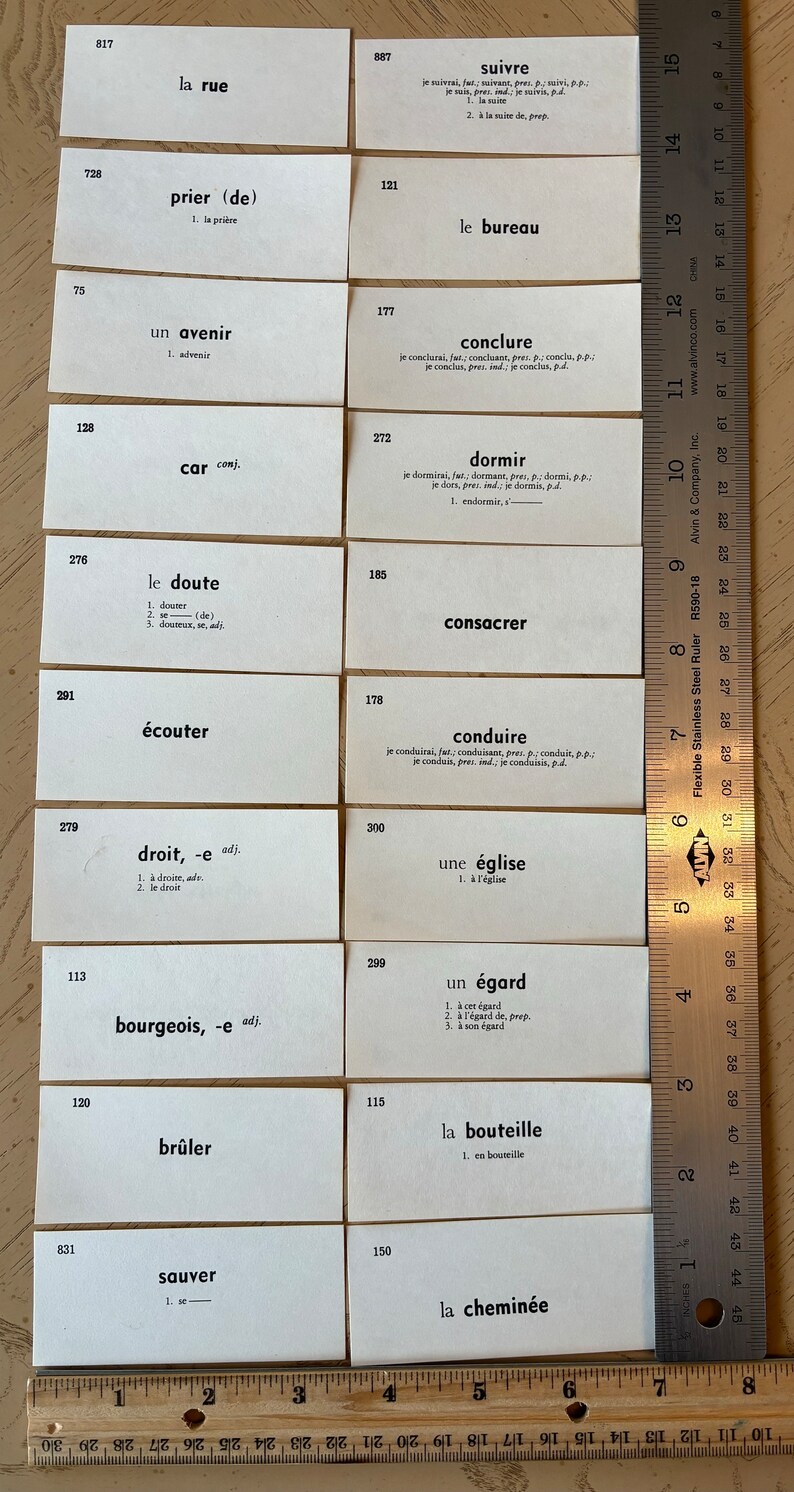 Op de afbeelding: Een set witte indexkaarten met Franse woorden en definities. De kaarten zijn genummerd en in rijen gerangschikt. De woorden zijn in zwarte inkt gedrukt. Een liniaal is zichtbaar aan de onderkant van de afbeelding.