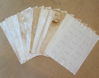 May include: A collection of rectangular paper sheets with a stained, vintage appearance in shades of beige and brown. One sheet features printed words including Clarity, Creative, Thrive, Confident, Artistic, Thriving, Passion, Beautiful, Flow, I wonder, Flair, Radiant, Create, Curious, Gorgeous, and Make.