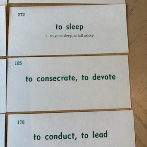 Op de afbeelding: Drie witte indexkaarten met groene tekst. De bovenste kaart heeft het nummer 272 en de tekst "to sleep". De middelste kaart heeft het nummer 185 en de tekst "to consecrate, to devote". De onderste kaart heeft het nummer 178 en de tekst "to conduct, to lead".