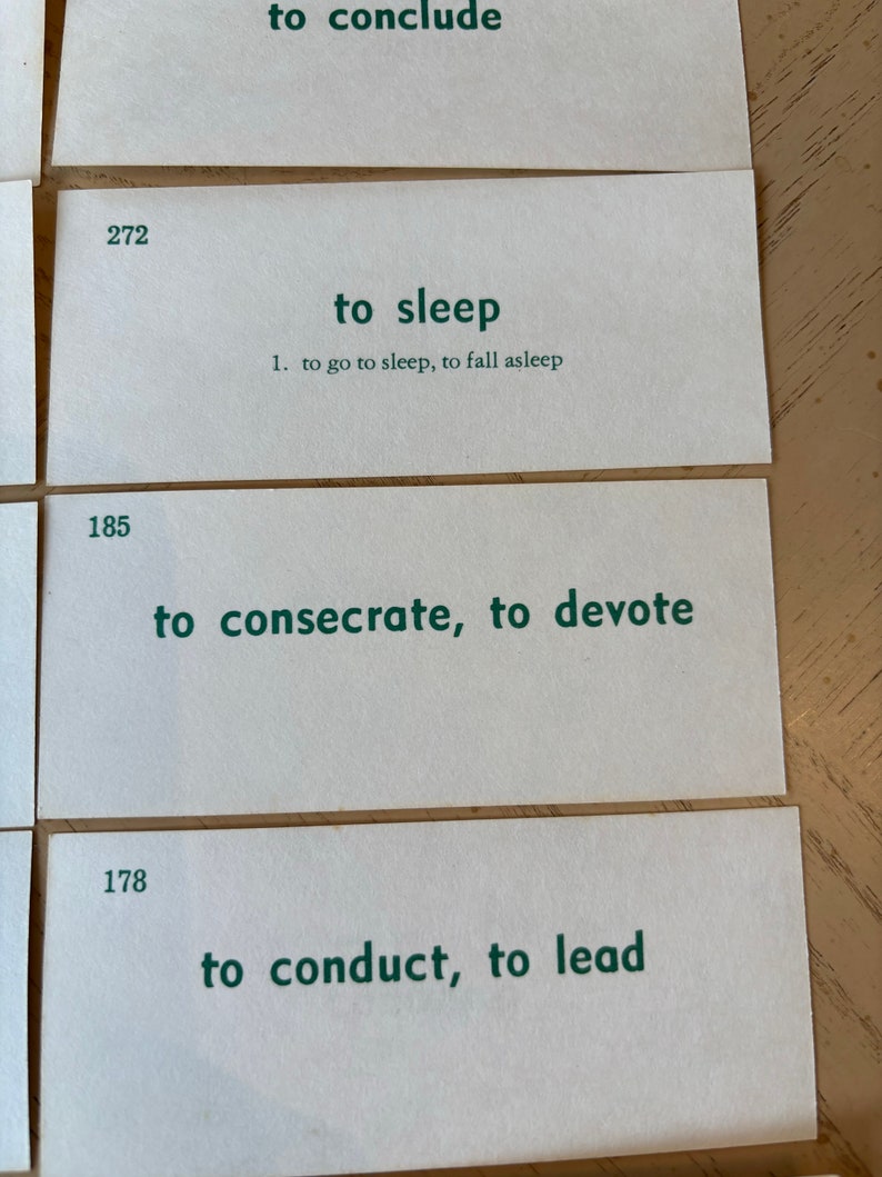 Op de afbeelding: Drie witte indexkaarten met groene tekst. De bovenste kaart heeft het nummer 272 en de tekst "to sleep". De middelste kaart heeft het nummer 185 en de tekst "to consecrate, to devote". De onderste kaart heeft het nummer 178 en de tekst "to conduct, to lead".