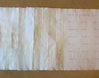 May include: A collection of rectangular paper sheets with a stained, tea-dyed appearance. One sheet features printed words including Beauty, Delightful, Joy, Bliss, Nature, Cherish, Abundance, Wonder, Dazzling, Breathe, Clarity, Calm, Ecstatic, Confidence, Radiant, Mindful, Passionate, Fabulous, Inspire, and Passion.