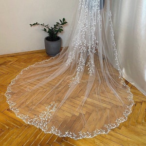 Könnte beinhalten: Ein weißer Braut Schleier mit einem zarten Blumenmuster. Der Schleier ist aus weichem Tüll und hat einen gewellten Rand.