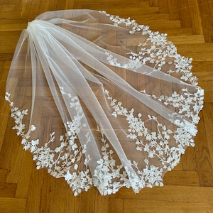 May include: A white bridal veil with delicate floral embroidery around the edge.