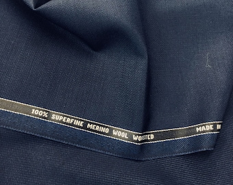 Puede incluir: Primer plano de una tela azul oscuro con textura tejida. La tela tiene una etiqueta que dice "100% Superfine Merino Wool Worsted Made In".