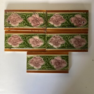 May include: Six rectangular tiles with a floral design. Each tile has a pink flower, green leaves, and a brown border. The tiles are arranged together, displaying the repeating pattern. The tiles are likely for decorative use.