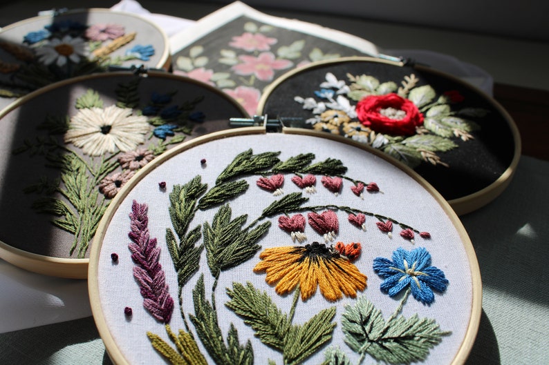 May include: Four embroidery hoops featuring floral designs. The hoops are made of wood and have white fabric stretched over them. The designs include a variety of flowers, leaves, and stems in shades of pink, red, yellow, blue, and green.