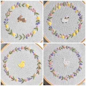 以下が含まれることがあります： 春をテーマにしたデザインの刺繍フレーム4つ。各フレームには、ウサギ、羊、ひよこ、ガチョウの画像を中心に、黄色、紫、ピンクの花のリースが描かれています。刺繍は明るい色の生地に施されています。