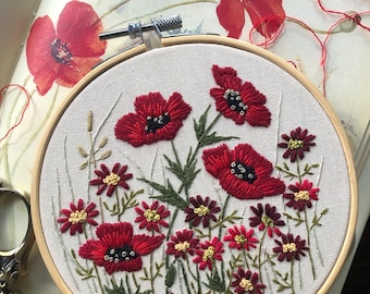 May include: Embroidered hoop art featuring red poppies and smaller red and burgundy flowers with green stems on a white fabric background.