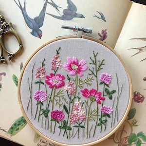 May include: Embroidered hoop art featuring a floral design with pink and green flowers on a beige fabric background. The hoop is made of wood and has a diameter of approximately 8 inches.