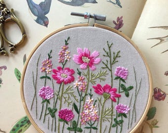 May include: Embroidered hoop art featuring a floral design with pink and green flowers on a beige fabric background. The hoop is made of wood and has a diameter of approximately 8 inches.
