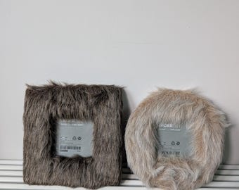 May include: A square dark brown faux fur picture frame and a circular light beige faux fur picture frame. Both frames feature a central glass pane with visible IKEA branding and product information printed on the surface of the glass inserts.
