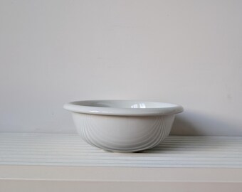 May include: A white ceramic bowl with a smooth, rounded rim and a deep, curved basin. The exterior surface features subtle, vertical ribbed detailing that wraps around the entire circumference of the bowl, creating a clean and uniform appearance.
