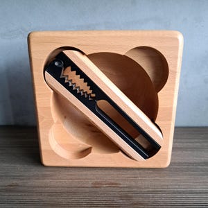 Peut inclure: Casse-noix en bois avec un mécanisme de casse en métal noir et argenté. Le casse-noix est placé dans une base en bois clair avec une indentation en forme de bol. Le design est simple et fonctionnel, adapté pour casser les noix.
