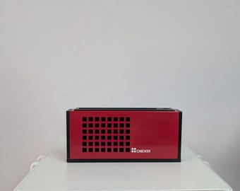 May include: A rectangular red radio with a black frame and a black speaker grille featuring a grid pattern. The word CHECKER is printed in white on the lower right side of the front panel, accompanied by a small square logo icon.