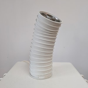 May include: A white, flexible lamp with a corrugated design. The lamp has a silver metal interior and is slightly bent. The lamp is on a white surface and has a white cord.