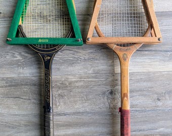 May include: Two vintage tennis rackets with wooden presses. The left racket is black with the text Dunlop and Avento on the green press. The right racket is natural wood with a Trophy logo and a red grip. Both feature metal hardware and strings.