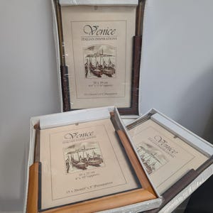 Peut inclure: Trois cadres photo rectangulaires sous emballage plastique protecteur. Chaque cadre présente un passe-partout crème avec le texte Venice Italian Inspirations et une illustration de gondoles. Les cadres varient en taille, incluant 20 x 25 cm et 20 x 30 cm.