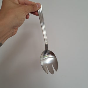 Pode incluir: Uma colher de servir salada de prata com um cabo longo e três pontas na extremidade.