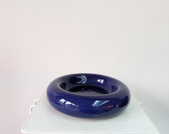 May include: A deep navy blue ceramic bowl with a smooth, glossy finish and a thick, rounded, doughnut-shaped rim. The bowl features a wide, circular opening and a flat, recessed centre, presenting a solid, uniform colour throughout its surface.
