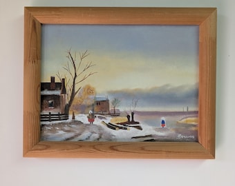May include: A framed landscape painting depicting a winter scene with a snow-covered path, a dark building, bare trees, and two small figures in traditional clothing near a body of water. The artwork is enclosed in a light-coloured wooden frame.