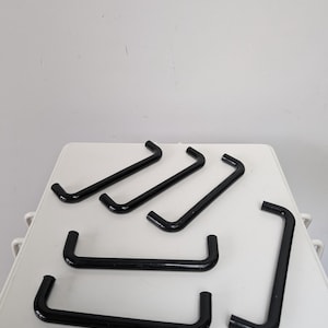 May include: Eight black plastic cabinet handles with a rounded rectangular shape. The handles are arranged in a random pattern on a white surface.