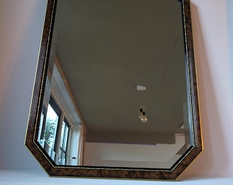 May include: An octagonal wall mirror featuring a dark brown, wood-grain patterned frame with thin gold-toned inner and outer trim accents. The mirror glass has bevelled edges and reflects the interior room environment.