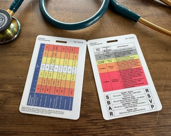 May include: Two white medical reference cards with color-coded charts and text, including "NEWS 2" and "SBAR" information, lie on a wooden surface. A stethoscope with a gold bell and dark green tubing is partially visible in the background.
