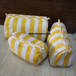 May include: Three quilted cosmetic bags in varying sizes. The bags feature a yellow and white striped pattern. Each bag has a zipper closure. The text "thekanthafabricshop" is visible on the bags.