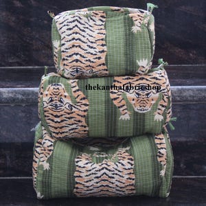 Puede incluir: Tres bolsas de tela apiladas, de color verde y naranja, con un diseño de estampado de tigre. Las bolsas tienen un cierre de cordón y están hechas de una tela suave y acolchada.