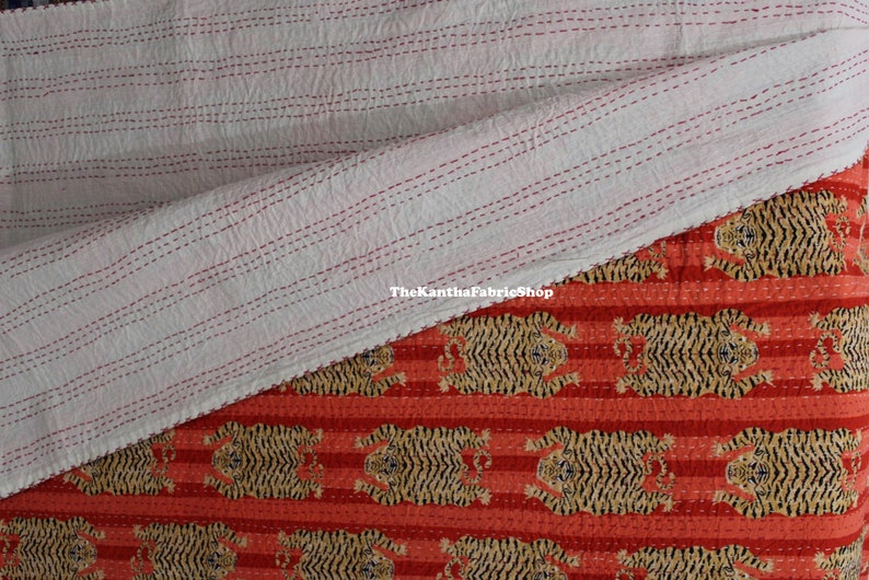 May include: A red and white striped kantha quilt with a tiger print design. The quilt is folded in half, showing the white side with red stitching. The text "TheKanthaFabricShop" is visible on the white side.