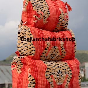 May include: Three quilted fabric storage bags featuring a tiger print design. The bags are stacked on top of each other. The top bag is red with a white tiger print, the middle bag is orange with a black tiger print, and the bottom bag is red with a white tiger print. All bags are quilted and have a zipper closure.