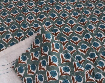 Puede incluir: Una colcha acolchada con un estampado floral repetitivo. El diseño presenta flores de color azul verdoso con tallos y hojas marrones sobre un fondo verde apagado. La colcha está cosida con hilo blanco.