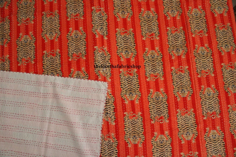 May include: A red and white kantha quilt with a repeating pattern of tigers. The quilt is made of cotton and has a hand-stitched design. The quilt is reversible, with a white side and a red side.