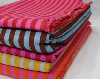 May include: A stack of folded fabric pieces featuring various striped patterns in vibrant colors including pink and red, brown and light blue, magenta, yellow and gray, and orange and pink. The text thekantbafabricshop is visible on the fabric.