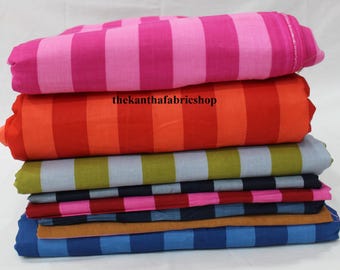 Puede incluir: Una pila de rollos de tela doblados con varios patrones de rayas en colores vibrantes que incluyen rosa fuerte, naranja, verde oliva, azul marino y azul claro. El texto thekanthafabricshop está impreso en negro sobre la tela naranja.