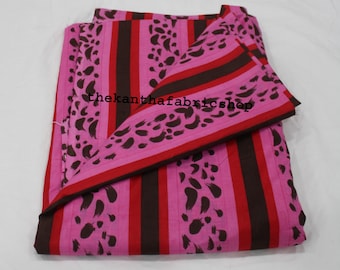 May include: Pink fabric with vertical brown and red stripes, and brown abstract shapes. The fabric has a folded edge with a red border and the text "thekanthafabricshop".