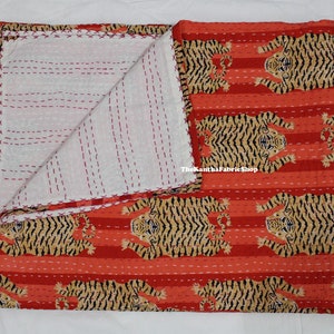 May include: A red and white kantha quilt with a tiger print. The quilt is folded in half and has a white background with red stitching. The quilt is made of cotton and is approximately 60 inches by 90 inches.