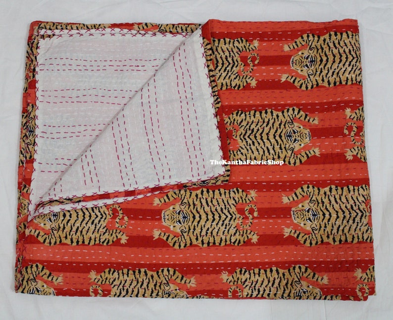 May include: A red and white kantha quilt with a tiger print. The quilt is folded in half and has a white background with red stitching. The quilt is made of cotton and is approximately 60 inches by 90 inches.