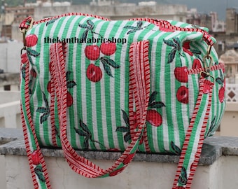 Puede incluir: Un bolso tote a rayas verdes y blancas con un estampado de cerezas. El bolso tiene correas y ribetes rojos. El texto "thekanthafabricshop" está impreso en el bolso.