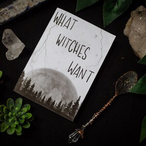 Könnte beinhalten: Eine weiße Karte mit dem Text "What Witches Want" in schwarzer Schrift. Die Karte zeigt ein Schwarzweißbild eines Vollmonds und Bäumen im Hintergrund.