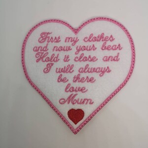 May include: Pink heart-shaped felt patch with white embroidery. The text reads "First my clothes and now your bear Hold it close and I will always be there love Mum". A small red heart is embroidered at the bottom.