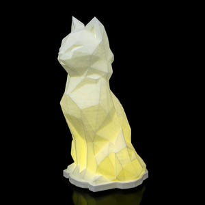 Pode incluir: Uma lâmpada de gato branca, de design geométrico, com um brilho amarelo quente. A lâmpada é feita de um material impresso em 3D e tem um acabamento liso e fosco.