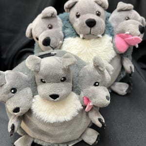 May include: A plush toy featuring a multi-headed creature with gray fur, black noses, and pink tongues. The toy has a white fluffy chest and a blue-green collar. The heads have small, round eyes and floppy ears. The toy is designed to resemble a mythical creature.