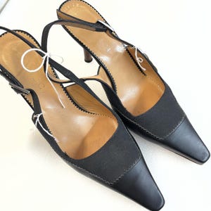 Peut inclure: Une paire d'escarpins noirs à bride arrière et bout pointu. Les chaussures présentent un empiècement en tissu et des détails en cuir, avec une fine bride et une fermeture à boucle. Les talons sont de couleur marron foncé.