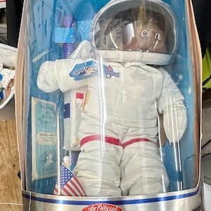 May include: A vintage Cabbage Patch Kids Young Astronaut doll in its original packaging. The doll is wearing a white spacesuit with red accents and a clear helmet. The packaging features a blue starry background and the words "Out of this World!"