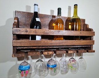 May include: A rustic wooden wall-mounted wine rack with two shelves and a bottom row of six glass holders. Three bottles of wine are displayed on the top shelf, and five wine glasses hang from the bottom row.
