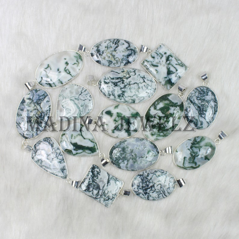 May include: A collection of gemstone pendants in various shapes, including oval, teardrop, and square. The pendants feature a white and green pattern, set in silver-colored metal. The image includes the text "MADINA JEWELZ".