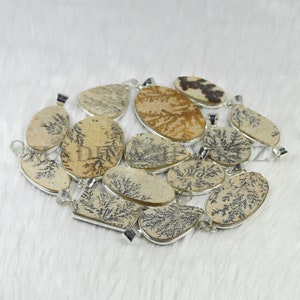 May include: A collection of 12 dendritic agate pendants with silver-tone bail settings. The pendants are various shapes and sizes, with a natural, earthy color palette of brown, tan, and black.